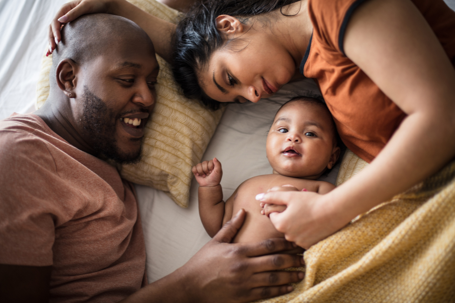 A family in bed, looking at a newborn baby